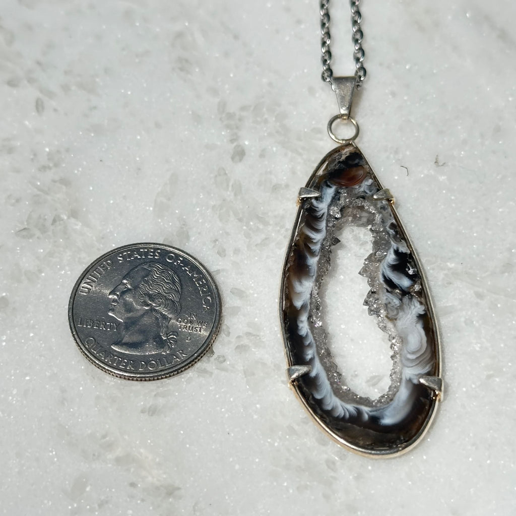 Agate geode slice crystal pendant next to a quarter for size reference 