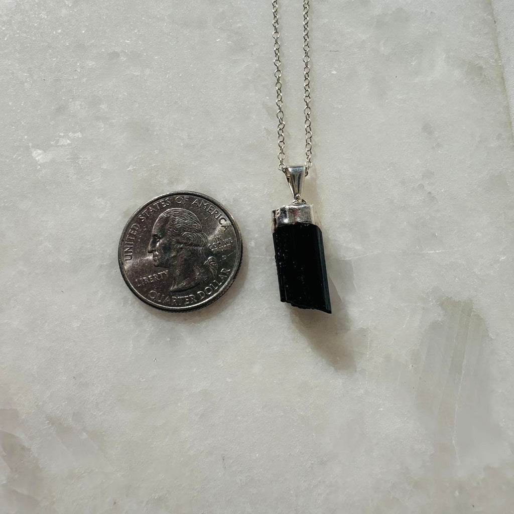 SIlver plated raw black tourmaline pendant necklace next to a quarter for size reference. 