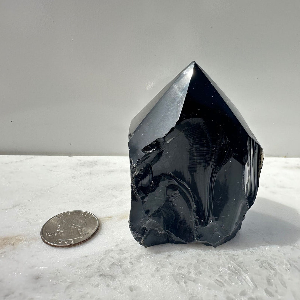 Black Obsidian Point next to quarter for scale