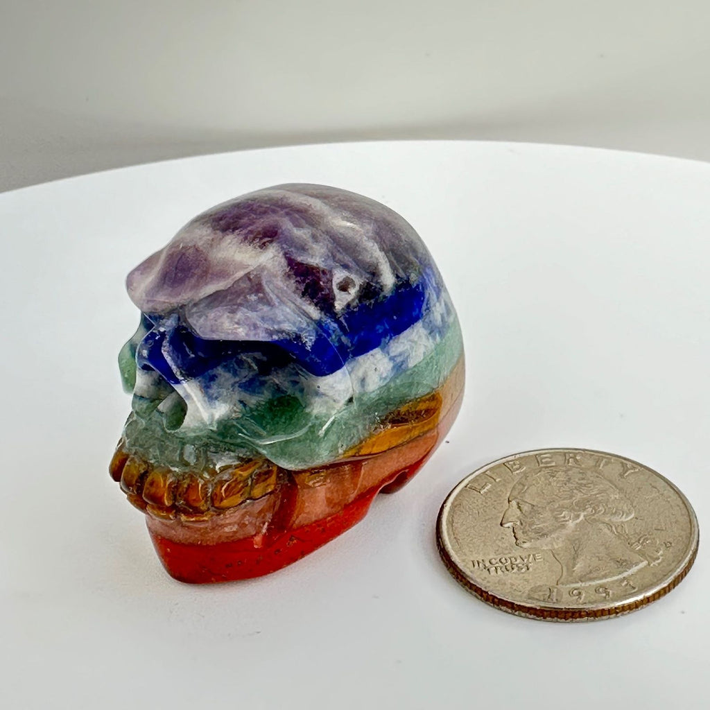 Chakra skull next to a quarter for size reference, made with 7 different crystals