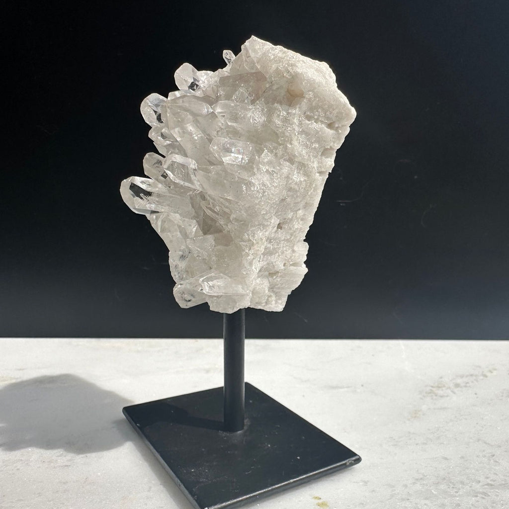 Side view of clear quartz cluster on a stand for home decor crystals