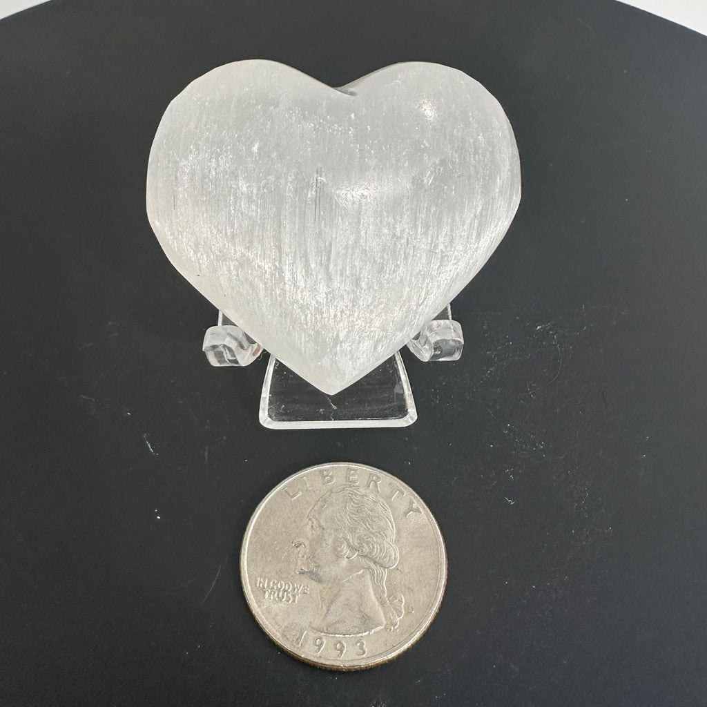 Selenite heart on a stand for display next to a quarter for size reference