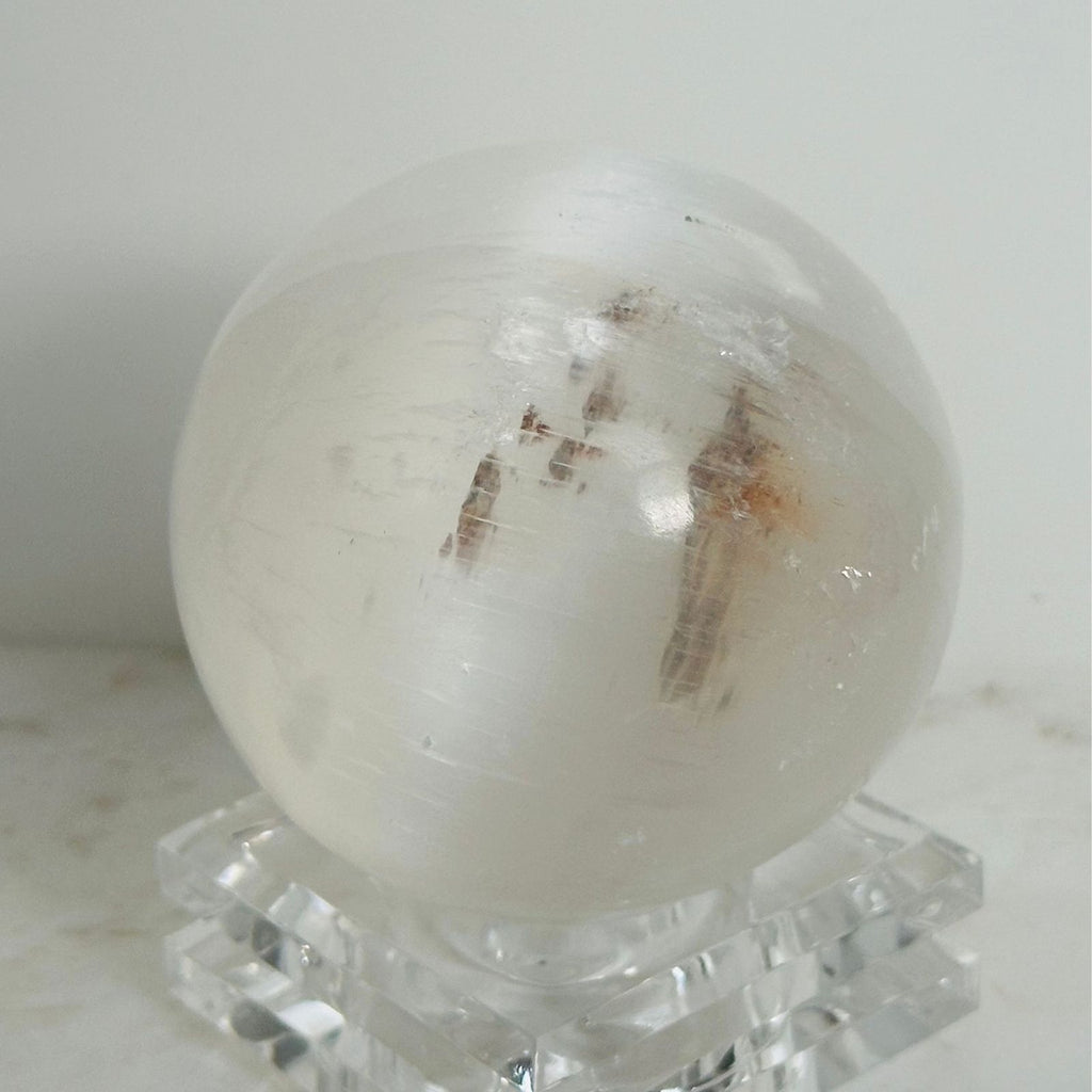 Selenite crystal sphere on white background with variations in inclusions