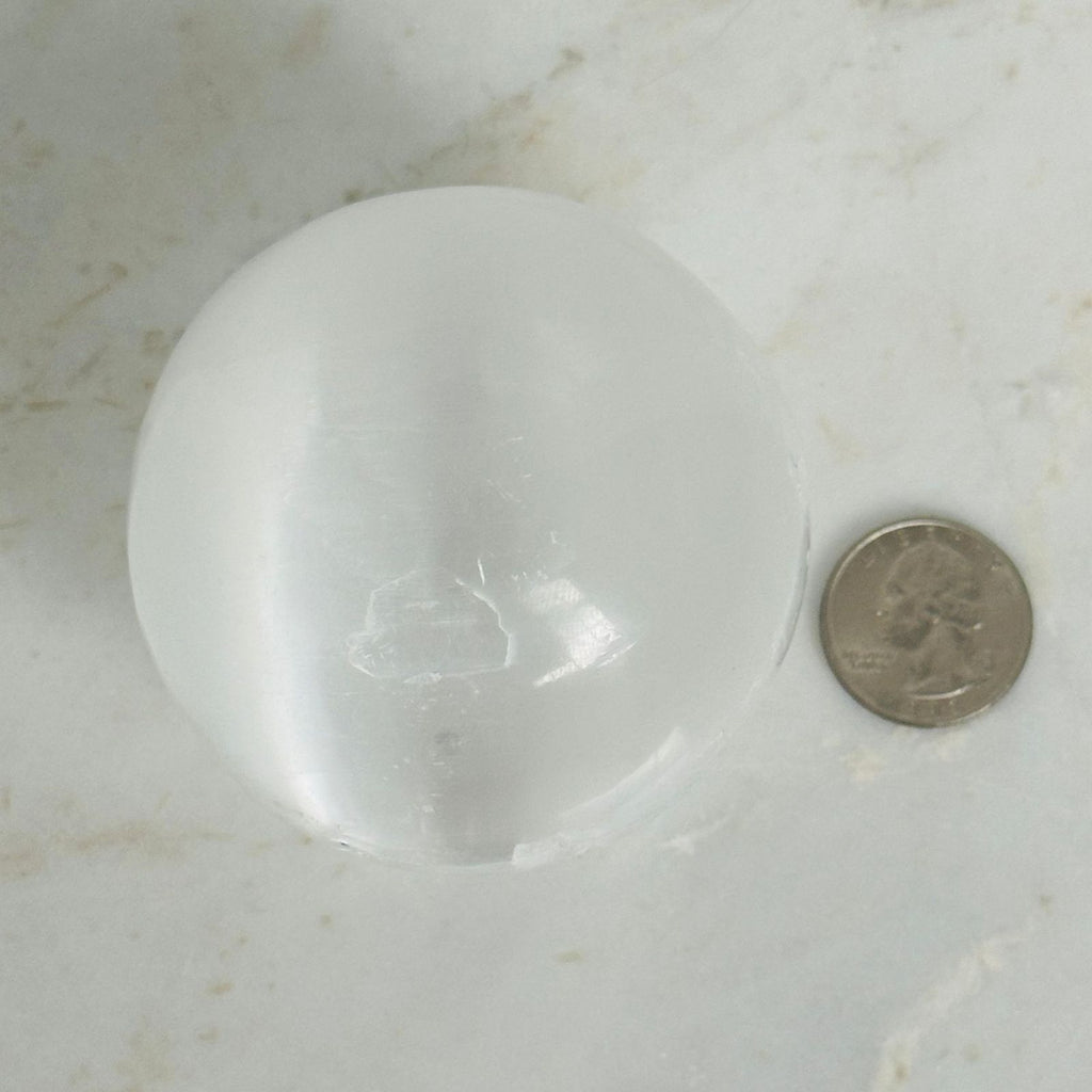 Selenite Sphere next to a quarter for size reference